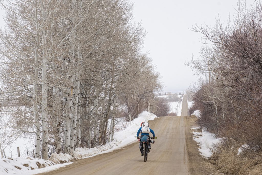 Riding down a gravel road with skis strapped to the bike.