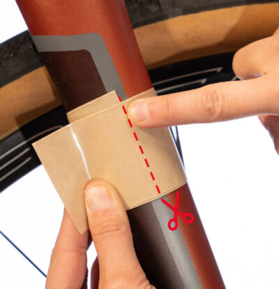 Clear protective tape being lined up on a carbon bike fork and a dotted line showing that it should be cut just before they overlap.