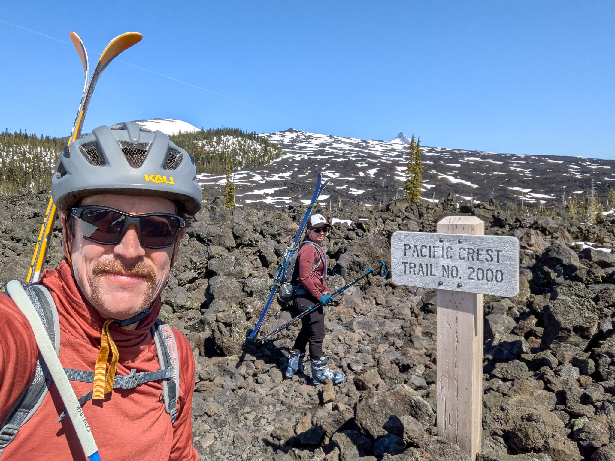 Chris and Katy hiking through a lava field carrying their skis.