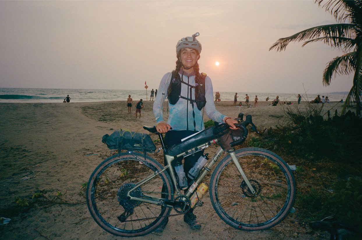 Poli standing with her bike at the beach after completing Le Tour De Frankie bikepacking race.
