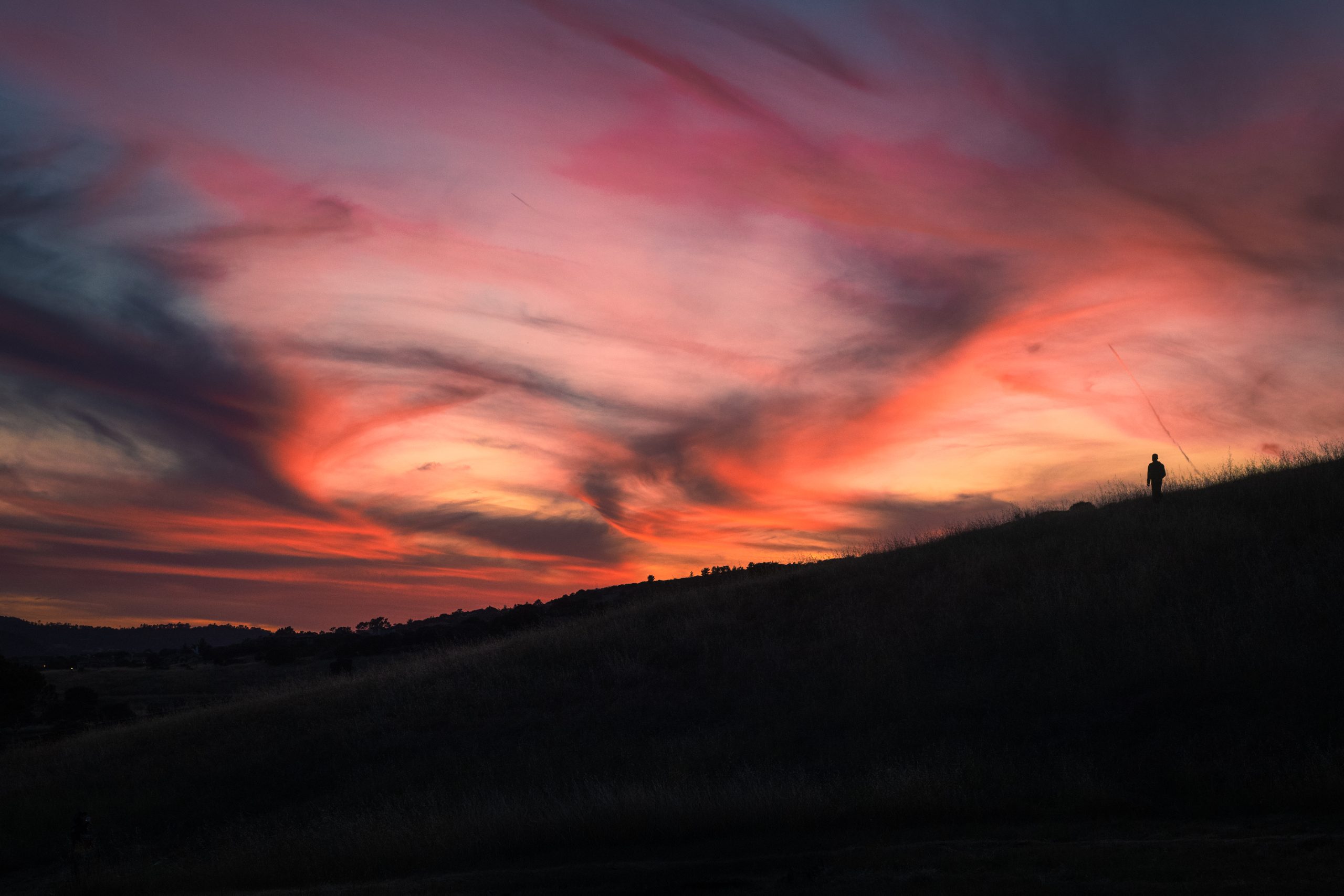 Pink and purple sky silhouetting a lone person standing on a ridge.