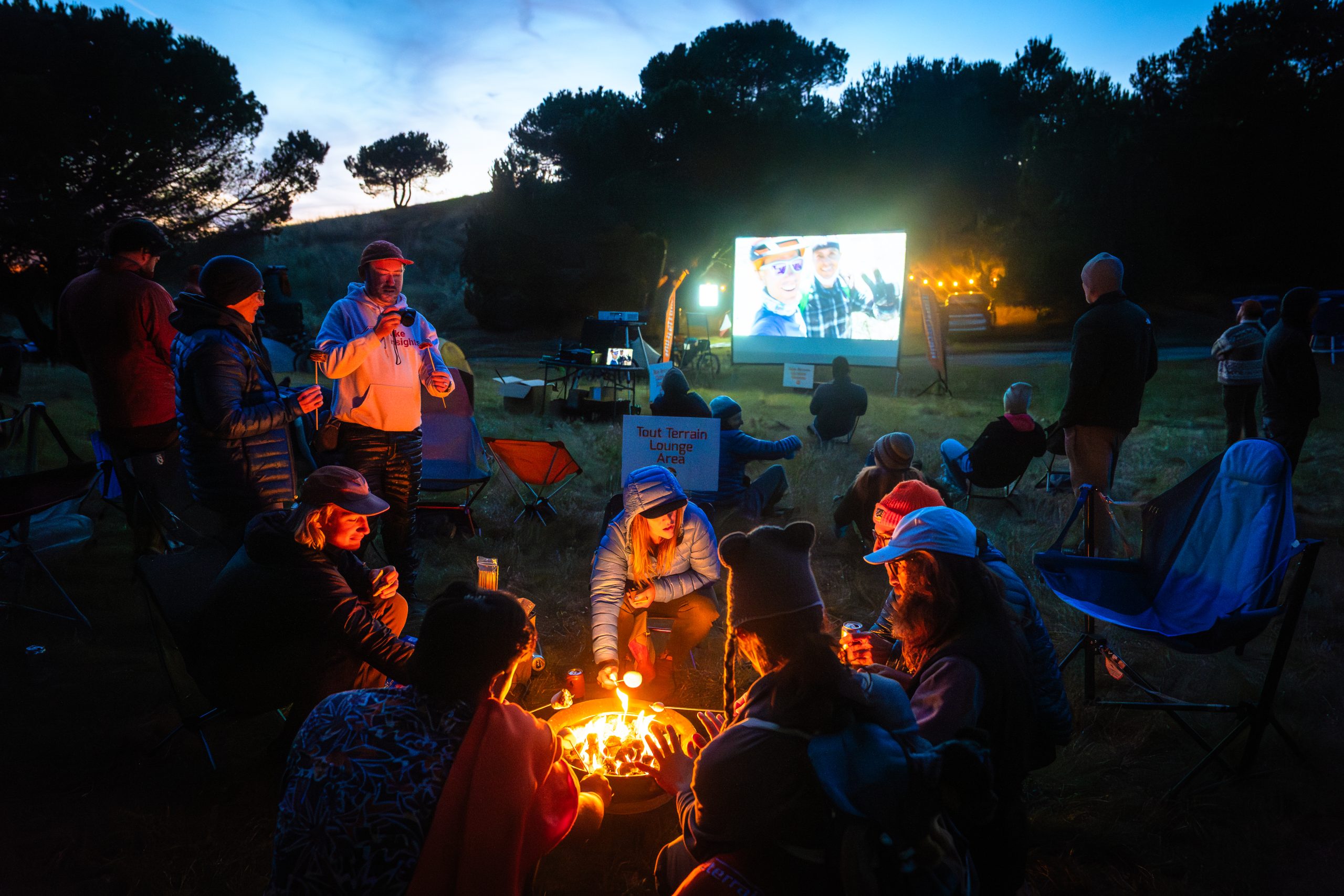 People making smores with movie playing on projector screen in the background.