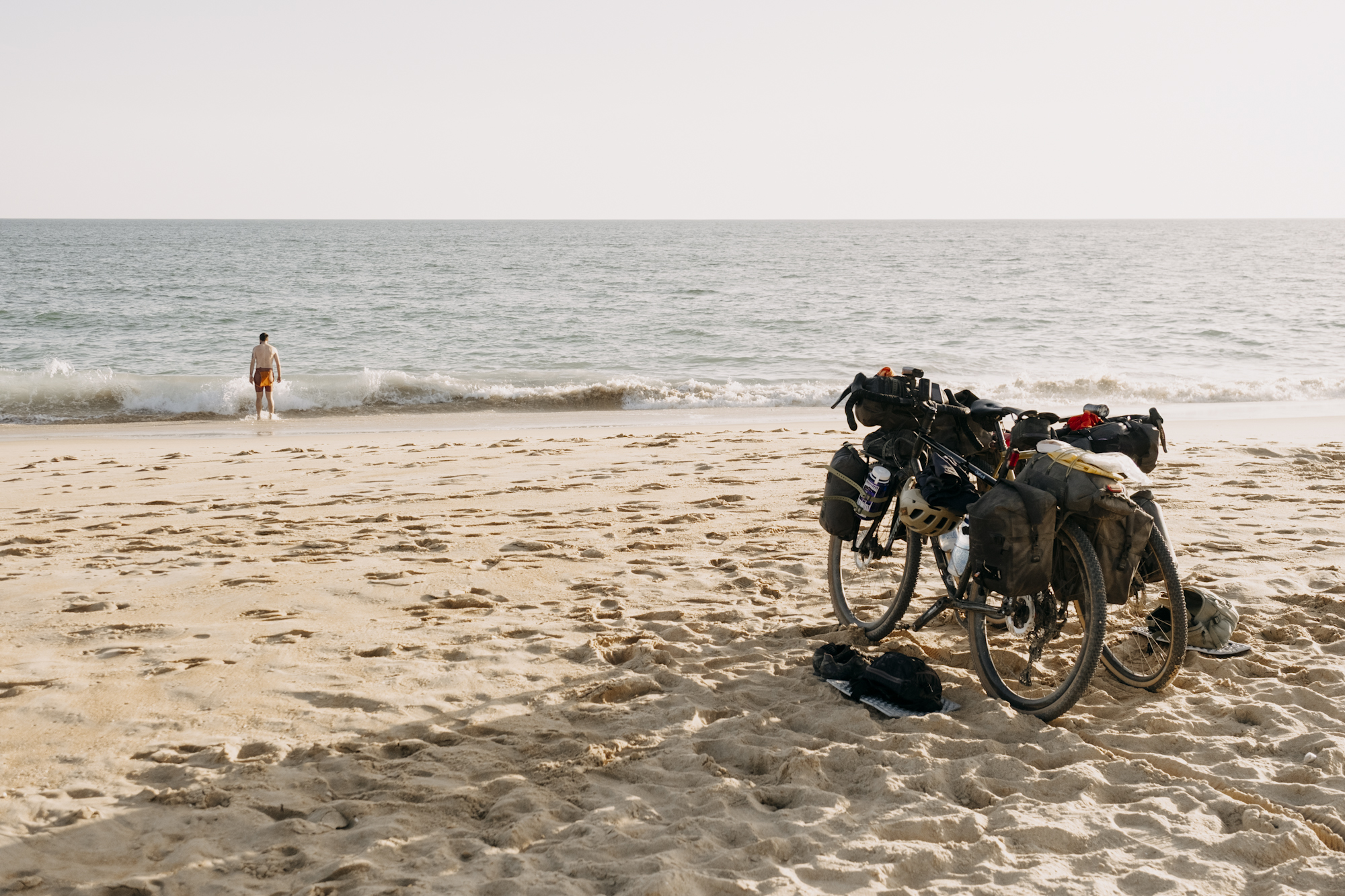 Angustias_Tour_TomasMontes-02 Javi standing by the sea with bikes in the sand behind him.